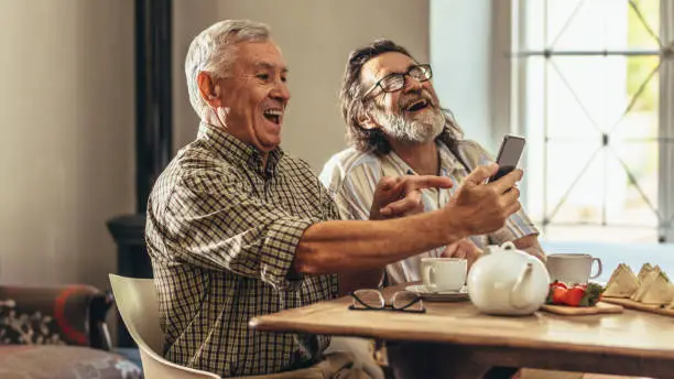 Photo of Two old men looking at old photographs together and laughing