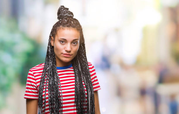 若い顔に真剣な表情で孤立した背景に髪アフリカ系アメリカ人女の子の編組。シンプルで自然なカメラを探しています。 - anger child braids braided ストックフォトと画像