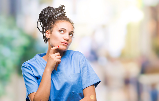 Young braided hair african american girl professional nurse over isolated background with hand on chin thinking about question, pensive expression. Smiling with thoughtful face. Doubt concept.