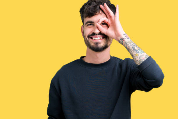 istock Young handsome man over isolated background doing ok gesture with hand smiling, eye looking through fingers with happy face. 1071468924