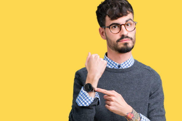 hombre inteligente guapo joven con gafas sobre fondo aislado de prisa hacia tiempo reloj, impaciencia, molesto y enojado para plazo demora - people waiting fotografías e imágenes de stock