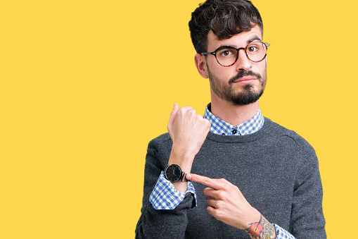 Young handsome smart man wearing glasses over isolated background In hurry pointing to watch time, impatience, upset and angry for deadline delay