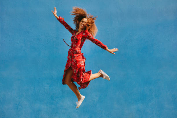 Beautiful woman in sundress jumping with joy Young female model in red sundress jumping with joy. Beautiful young woman jumping over blue background. woman in red dress stock pictures, royalty-free photos & images