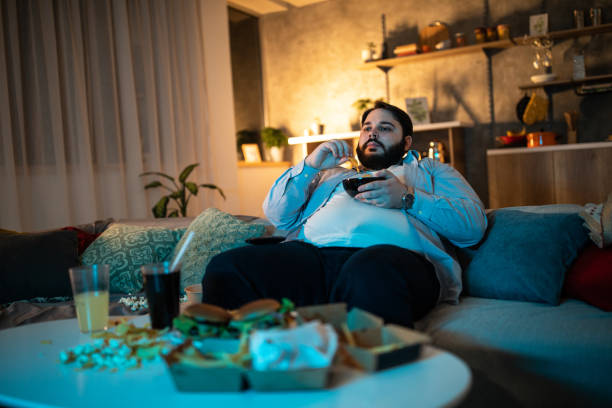 Overweight man watching TV Man eating potato chips  while watching movie on TV pot belly stock pictures, royalty-free photos & images