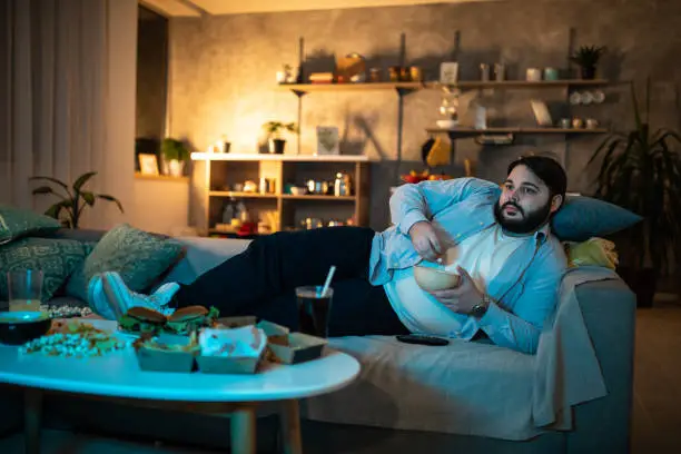 Lazy man lying on side on sofa and watching TV while eating popcorn