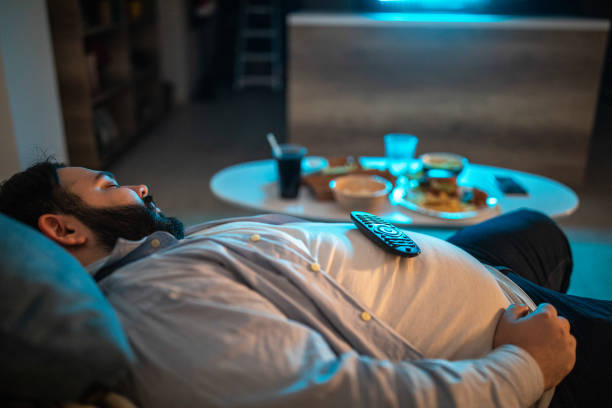 Lazy man fell asleep in living room Overweight man napping on couch at home in front of TV at night excess fat stock pictures, royalty-free photos & images