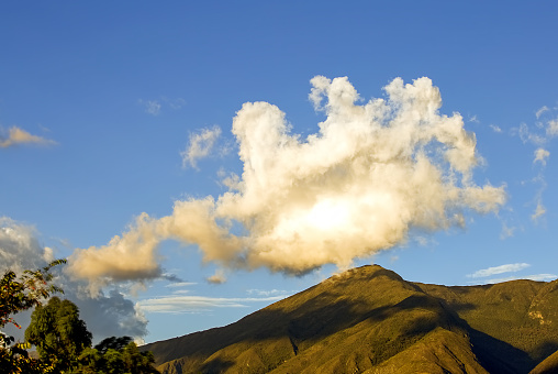 A white and yellow dense cloud seems to rise from the top of Iguaque mountain, at the Andean mountain range of Colombia.