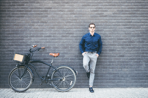 young businessman with  bicycle in front of brick wall