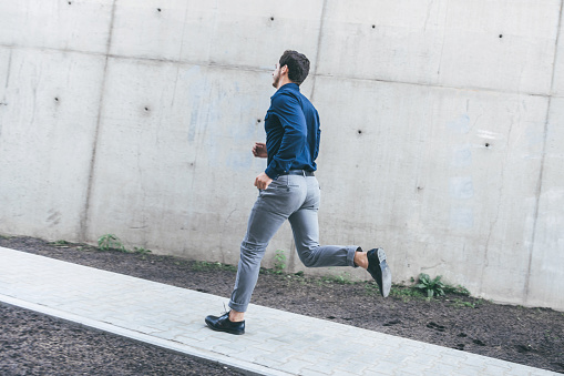 young businessman running outdoors in city in front of concrete wall