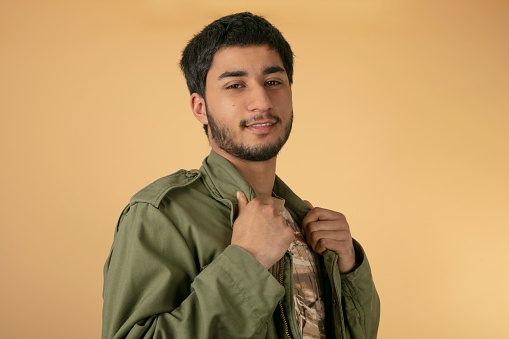 Young Man in green military Jacket on beige Background