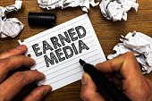 Text sign showing Earned Media. Conceptual photo Publicity gained through promotional efforts by multimedia Man holding marker notebook page crumpled papers several tries mistakes.