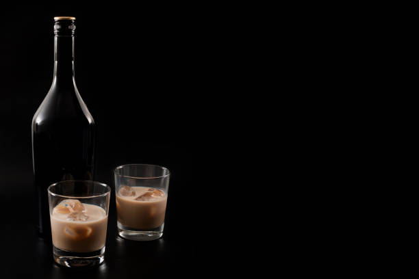 Coffee liqueur and alcoholic beverages based on milk and whiskey concept with Irish cream bottle and glasses with ice isolated on dark black background with copyspace