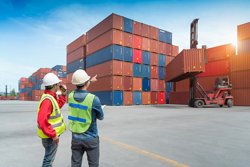 Foreman control loading Containers box from Cargo freight ship in Warehouse shipping transportation concept.