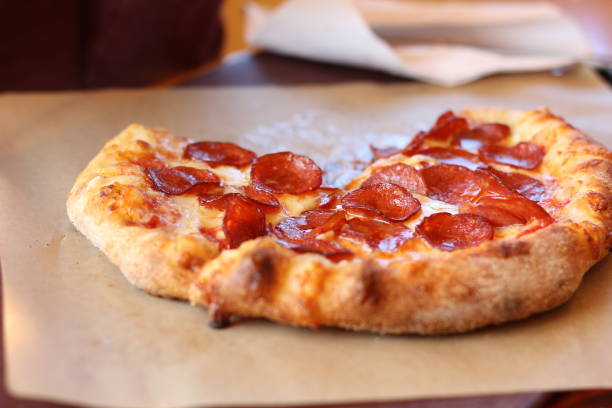 Delicious and greasy personal sized pepperoni pizza on brown parchment paper.