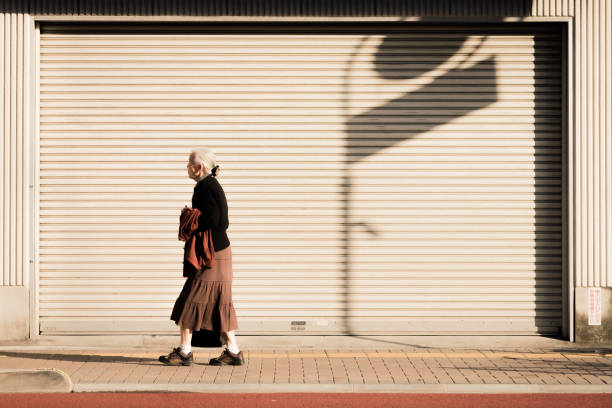 Aging population social issue of a widow lonely woman walking along the street of Japan JAPAN, TOKYO - NOVEMBER 2016: An unidentified old woman walks along the roadside of Tokyo, Japan. Japan's population is aging. aging population stock pictures, royalty-free photos & images