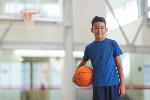 Boy with basketball A boy is standing in a gymnasium holding a basketball. He is smiling at the camera. youth basketball indoor stock pictures, royalty-free photos & images