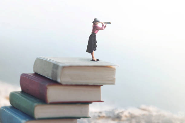 miniature woman looks at the infinity with the spyglass on a scale of books stock photo