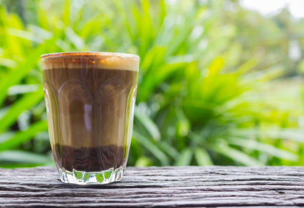 istock Latte Coffee in Glass on Wood Table with Natural Tree Background Eye Level Left 1071674306