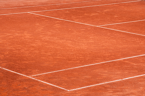 Part of empty used red clay tennis court playground surface with white lines closeup
