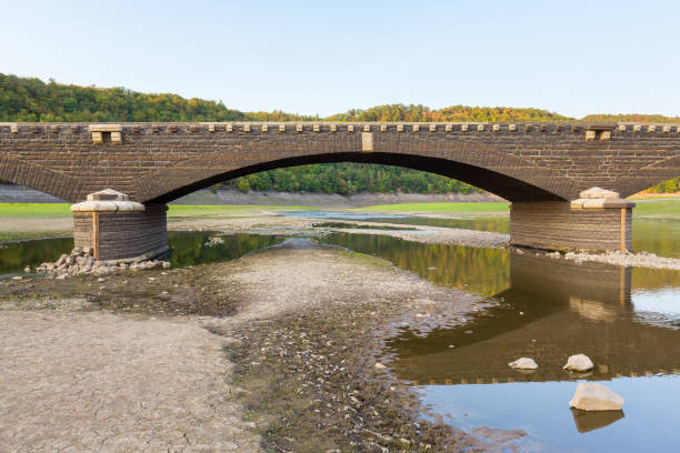 Stone arch bridge in dry german Edersee in Sauerland area. Here a beautiful landscape in the german Sauerland. Normally you can not see the riverbed here because it's all water of the Edersee in this valley. But because of the dry weather this summer the river bed is walkable and there is much lesser water. Many tourists came this summer to walk over this stone bridge because normally this bridge has disappeared under water!