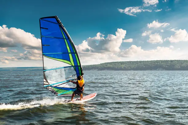 Photo of the man athlete rides the windsurf over the waves on lake