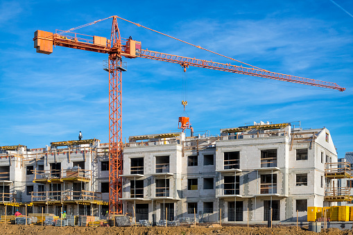 Tower crane and new building silhouettes under construction at construction site at white sky background