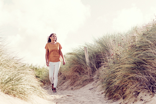 Woman walking through sand dunes at Fistral Beach, Newquay on a sunny Autumn day.