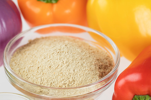 Nutritional yeast surrounded by other fresh ingredients for creamy vegan peppers and onions.