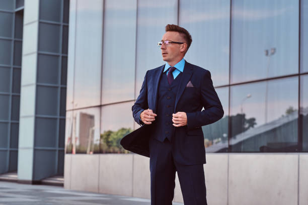 istock Confident businessman dressed in an elegant suit looking away and button up his jacket while standing outdoors against cityscape background. 1071808198
