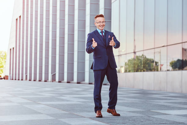 istock Joyful confident businessman dressed in an elegant suit shows gesture cool while standing outdoors against cityscape background. 1071808358