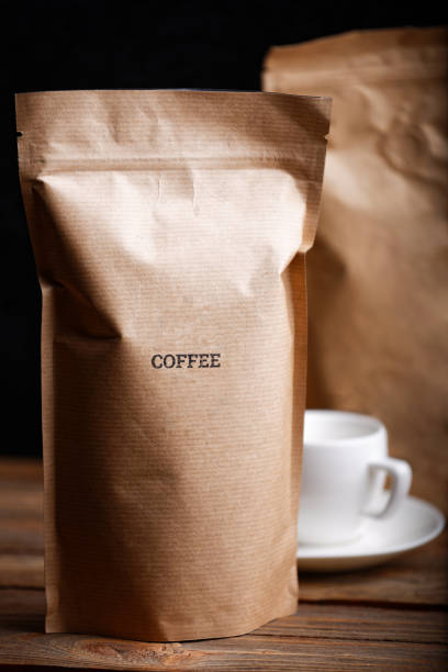 Brown craft paper bags with coffee beans on wooden table against black background