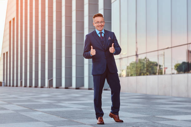 istock Joyful confident businessman dressed in an elegant suit shows gesture cool while standing outdoors against cityscape background. 1071808866