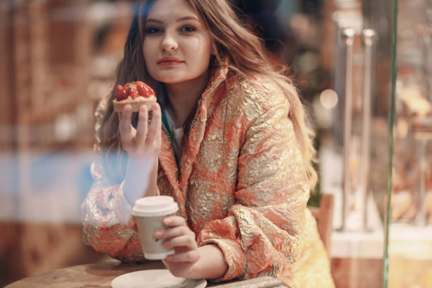 A young woman is sitting in a pastry shop cafe with coffee and cake.