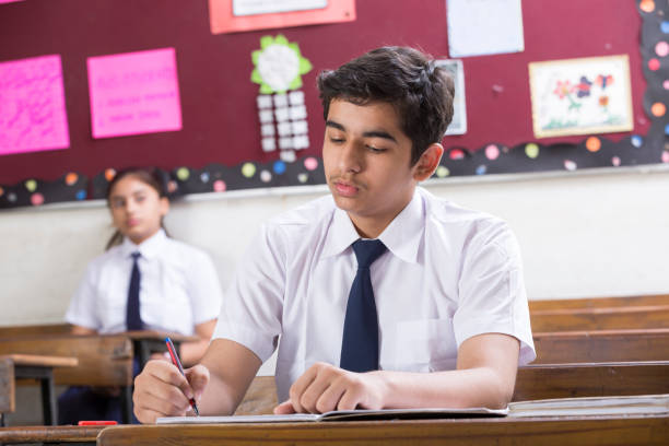 male student in classroom writing in notebook - Stock image