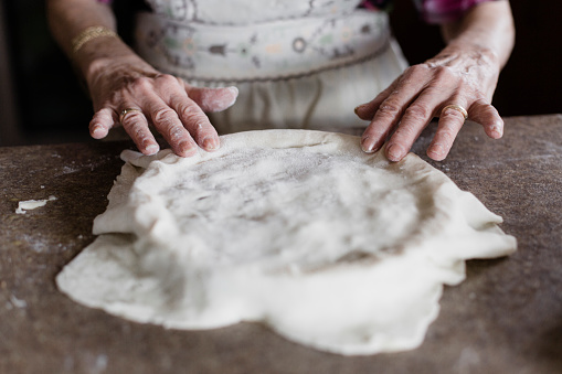 Close up of grandmother hands kneading on table in home kitchen. Retired elderly baker with bonete mixing ingredients with sifted wheat flour kneading for baking traditional cake and bread.