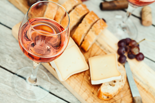 Two glasses of rose wine and board with fruits, bread and cheese on wooden table