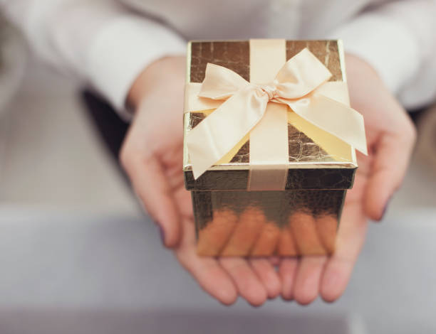 istock Female Hands Holding a Small Golden Box with a Bow on it 1071875408