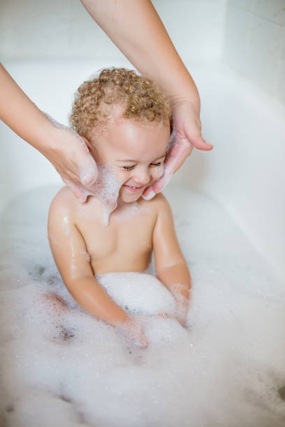 Cute two year old boy taking a relaxing bath with foam stock photo