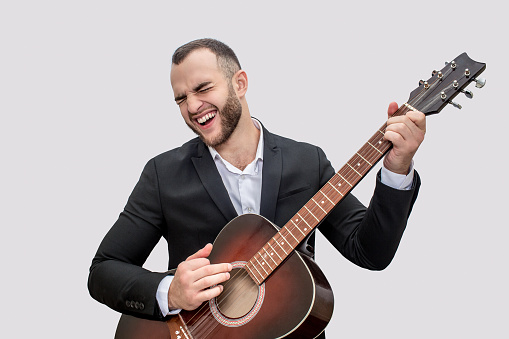 Singer in black suit stand and play on guitar. He sing song. Young man wears suit. Isolated on white background