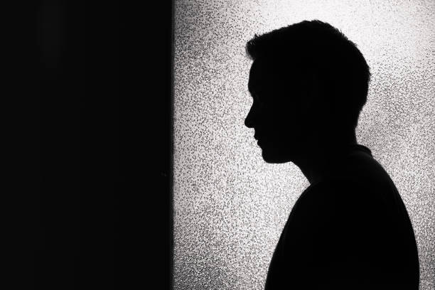 silhouette di giovane uomo premuroso in piedi in una stanza buia. - thinking young men indoors part of foto e immagini stock