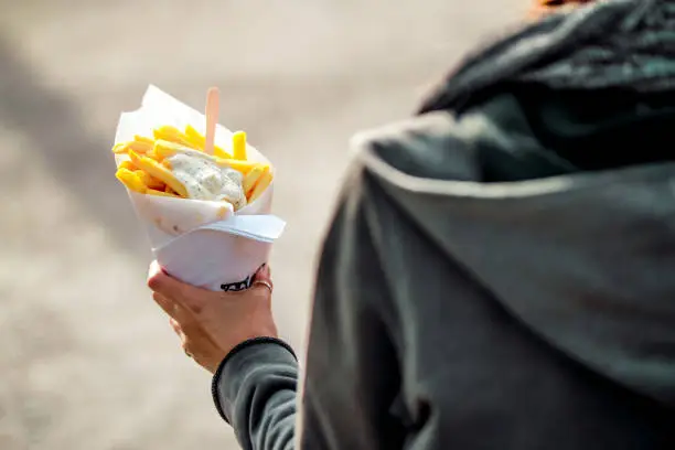 Photo of Brussels, Kingdom of Belgium. Tourist holds belgian fries in hand in the streets of Brussels. French Fries with mayonnaise.