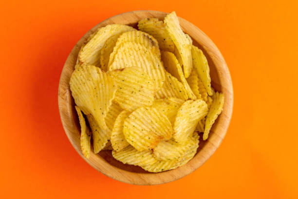 istock Crunchy corrugated potato chips in wooden bowl on bright orange background. 1071908450