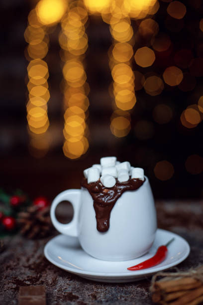 Portion of homemade chilli pepper hot chocolate in messy cup on a dark background with christmas lights.