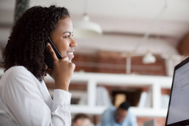istock Smiling black female employee talk on phone working at computer 1071915494