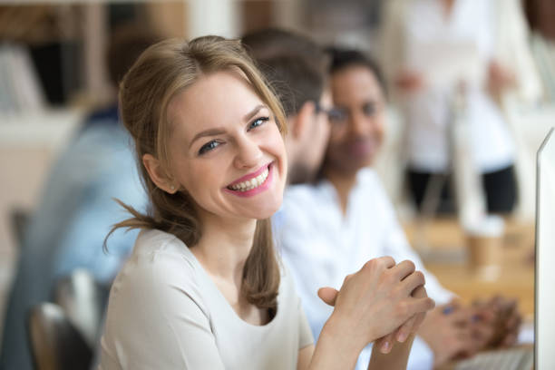 Portrait of smiling female employee posing at workplace Portrait of smiling millennial female employee looking at camera working at computer, happy woman posing for picture sitting in shared workplace, excited worker making photo in office trainee photos stock pictures, royalty-free photos & images