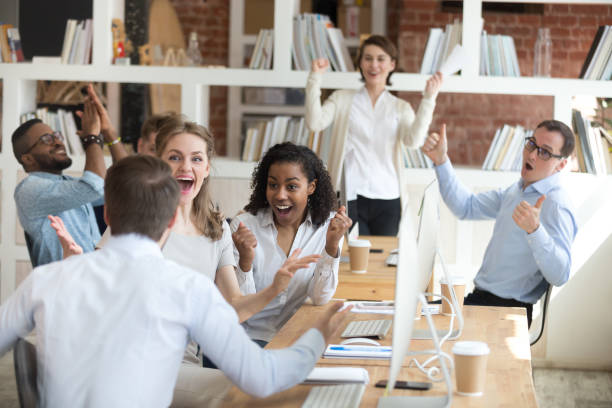 Male employee share good news with excited diverse colleagues Male worker share good news with multiracial colleagues in shared workplace, diverse employees scream with happiness excited with corporate success or goal achievement, team celebrating win sales win stock pictures, royalty-free photos & images