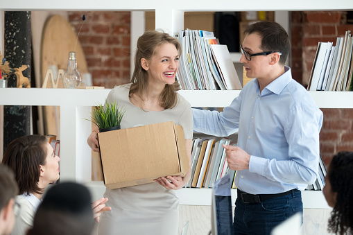 Businessman introduce excited female newcomer at corporate meeting to colleagues, male CEO presenting smiling employed woman or new employee with cardboard box in hands to coworkers. Hiring concept