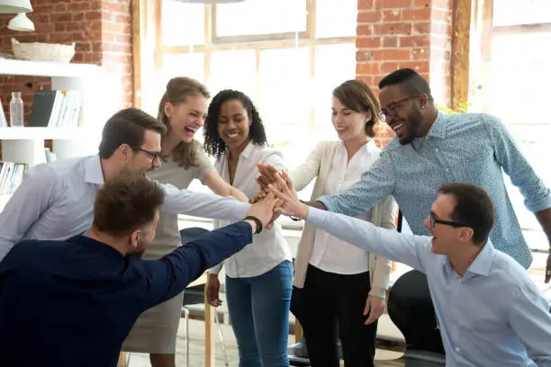 Photo of Excited diverse workers join hands at teambuilding activity