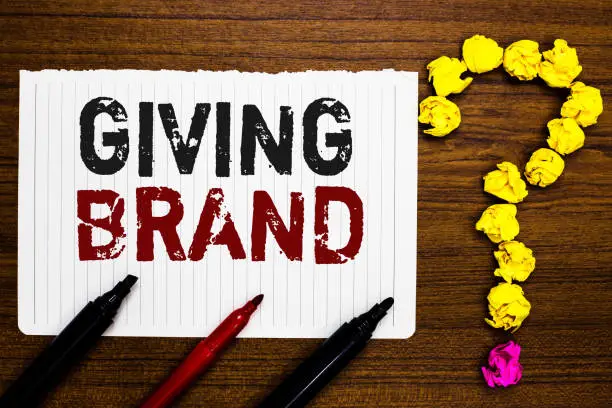 Photo of Handwriting text writing Giving Brand. Concept meaning The process of giving a Name to a company products or services Paper markers crumpled papers forming question mark wooden background.