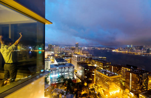 Businessman standing by the window with arms raised at night.